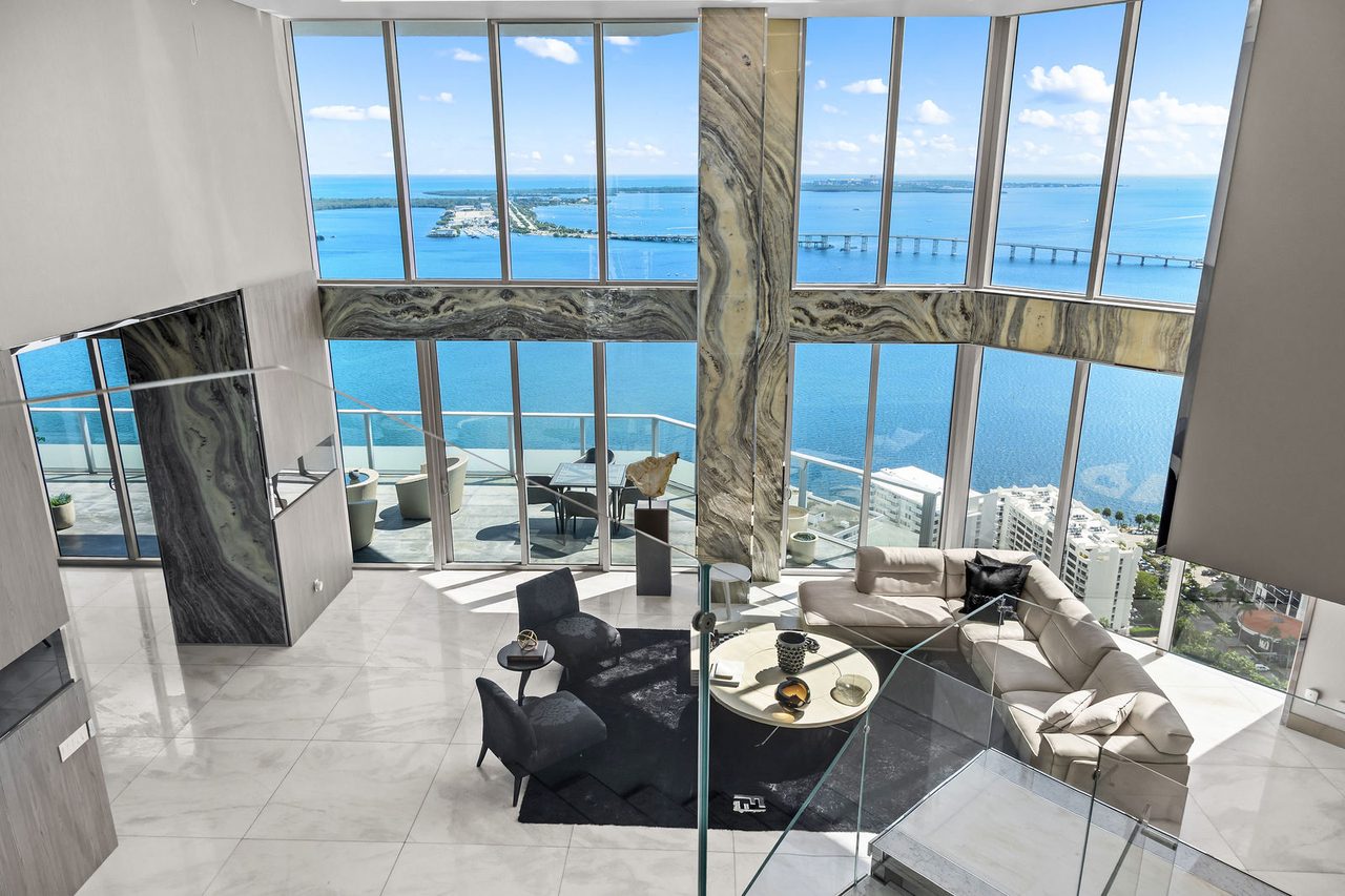 From the upper level: the double-height living room, glazed on three sides over Biscayne Bay